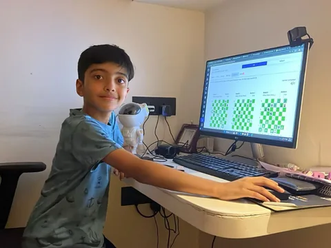 Dhruv at a desk playing chess on a computer during an online class