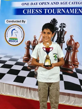 Reeyan holding a trophy in front of a chess tournament banner